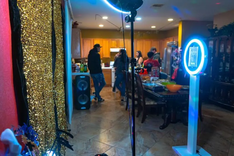 A photo booth station set up with back drop, some props, lights, and selfie station. In background a dozens of people.