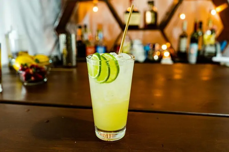 A cocktail on the table. Inside of cocktail some juice, liquor, lime, and ice.