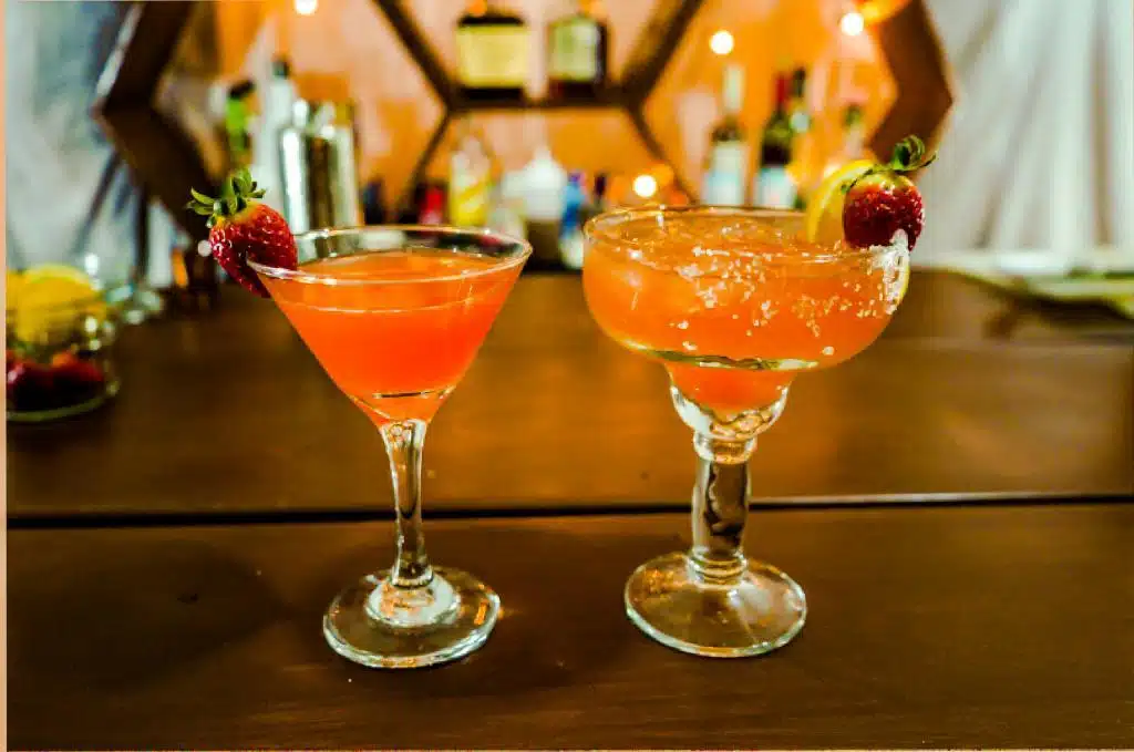 Two pink colored cocktails. They booth have strawberry decoration.