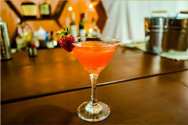 a pink color drink inside of a martini glass. It has a strawberry as decoration.