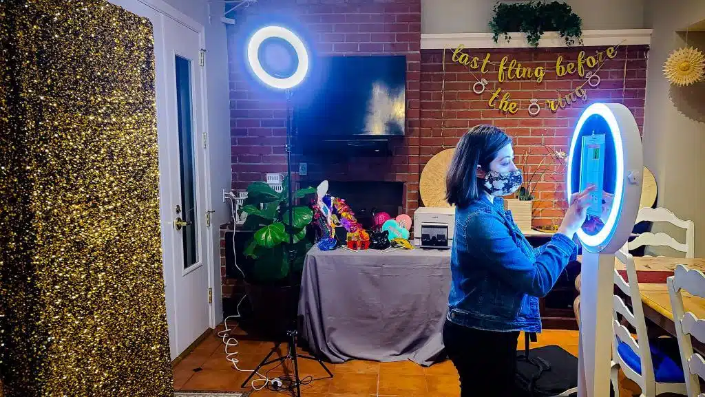 A female taking selfie using photo booth station. The station has backdrop, lights, props, and printer.